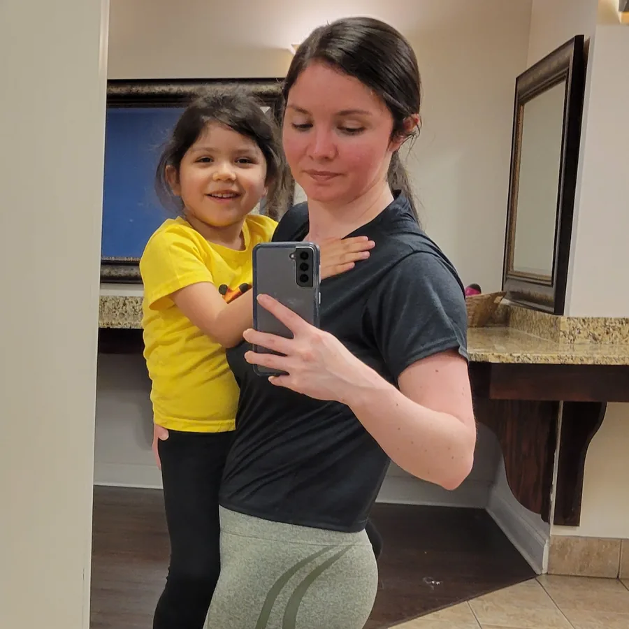 Mayra B carrying her young daughter on her hip, photographed in a mirror